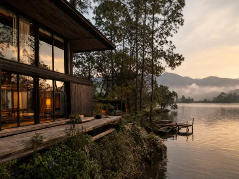 Casa Lago: residencia de madera carbonizada y vidrio entre pinos, con terraza y muelle propio sobre el lago de Valle de Bravo al atardecer, con bruma entre las montañas