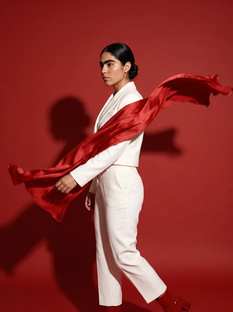 La estola de seda roja vuela alrededor de la modelo, frente a papel rojo
